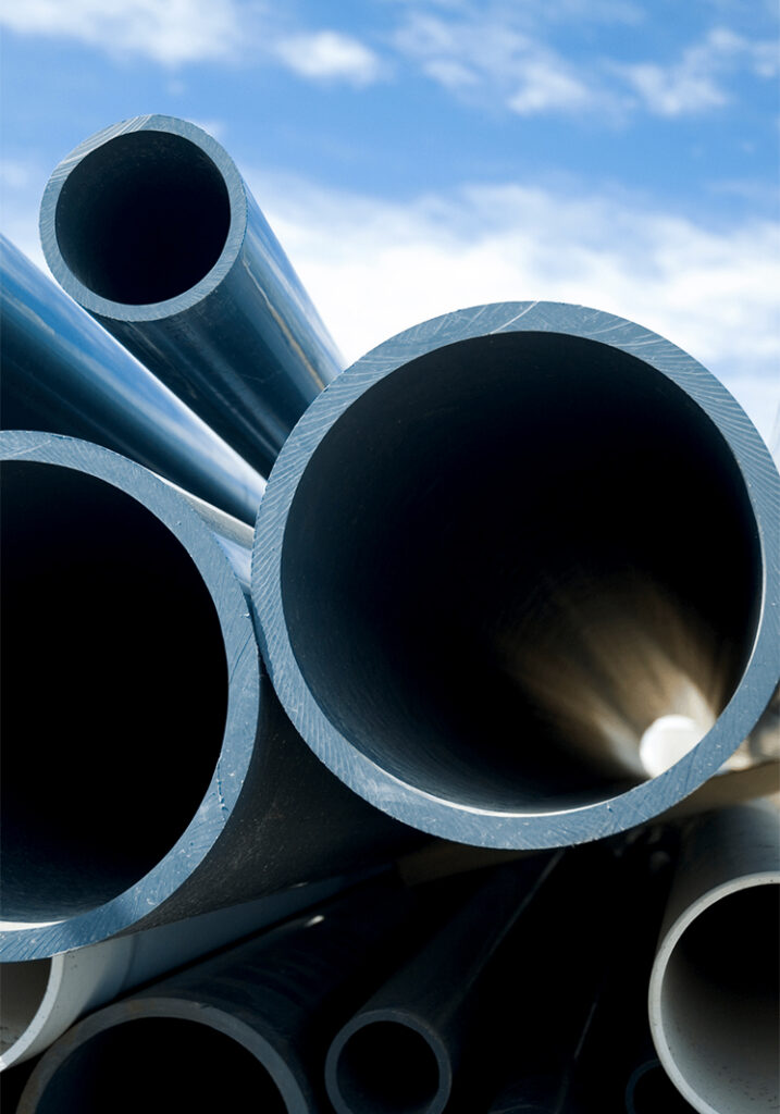 Close-up view of several large, stacked blue PVC pipes with a blue sky and white clouds in the background.