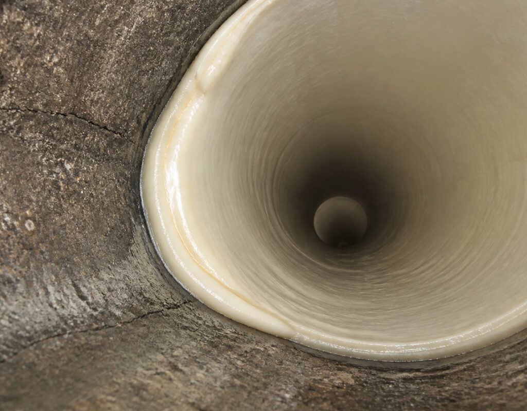 A close-up view looking down into a hollow, cream-colored tunnel or tube with textured walls, possibly made of natural or organic material.